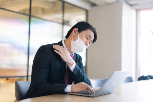 肩こりの原因、それは幽霊のしわざです〜会議中にマスク姿の男性が肩を押さえる