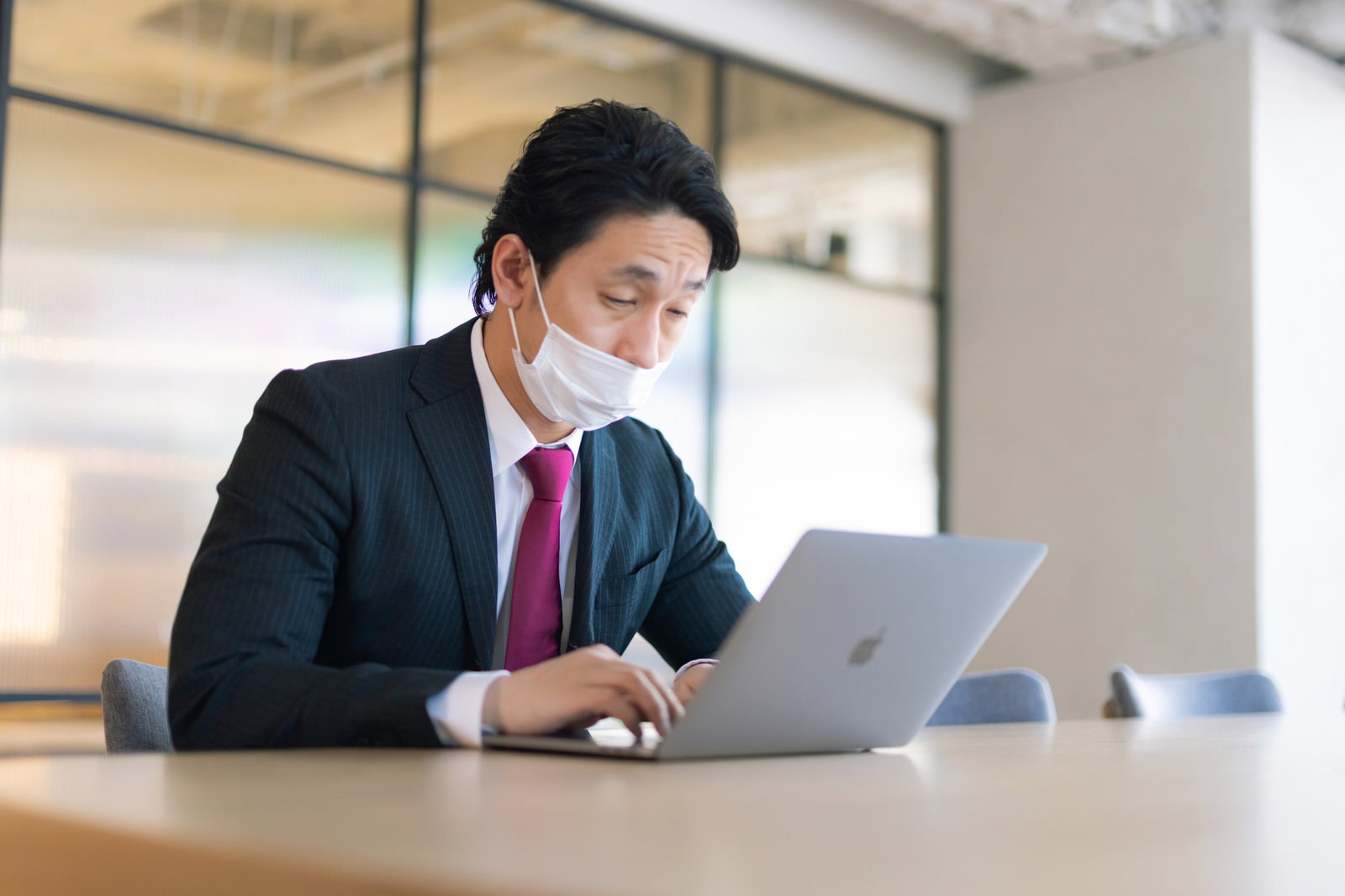 オフィスでマスクから鼻を出してノートパソコンで作業をする会社員男性［モデル：大川竜弥］