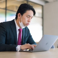 不満げな顔でノートパソコンの作業をするスーツ姿の会社員の写真