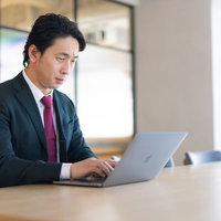 広い会議室でノートパソコンを使ってリモートワークする男性の写真