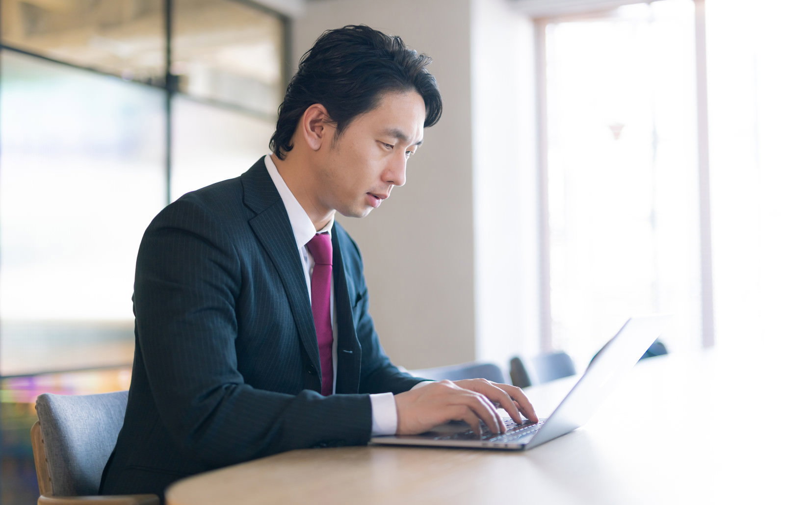 オフィスでノートパソコンを使って作業するスーツ姿の男性［モデル：大川竜弥］