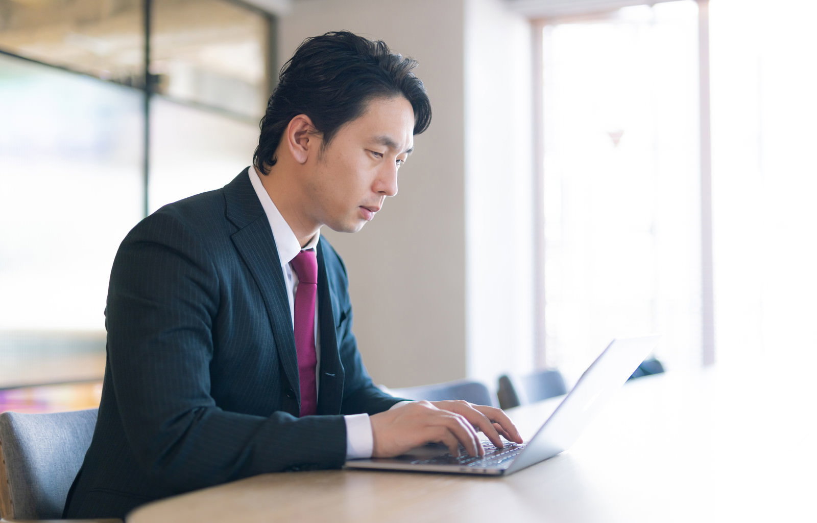 スーツを着たビジネスマンがオフィスのデスクでノートパソコンを使って作業している［モデル：大川竜弥］