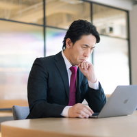 業績の下がり具合を懸念してデスクで考え込む役員の写真