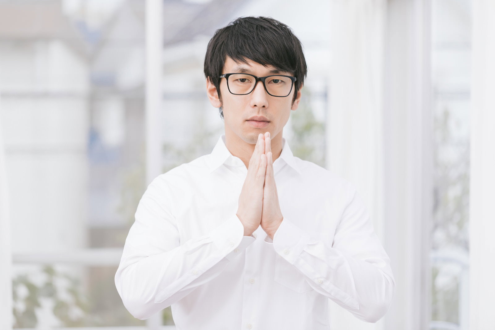 眼鏡の男性が無表情で両手を合わせて祈っている［モデル：大川竜弥］