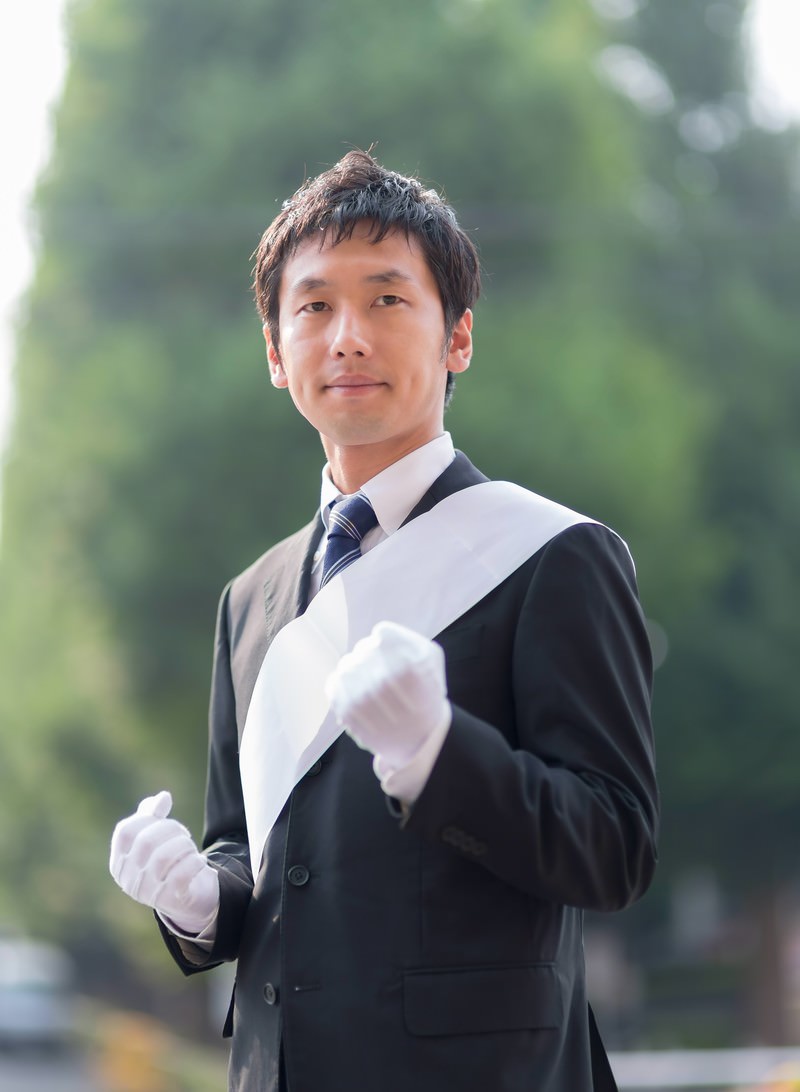 白い手袋と襟飾りの出馬したばかりの立候補者［モデル：大川竜弥］