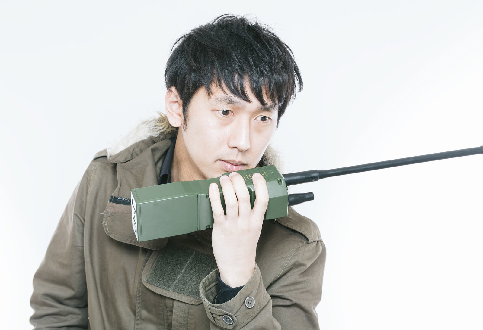 モッズコートを着た男性がトランシーバーを肩に担ぎ、目線を下ろしてうなだれた表情