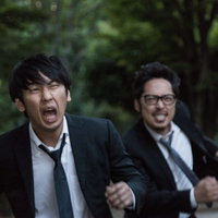 全力で容疑者を追いかけるスーツ姿の男性記者の写真