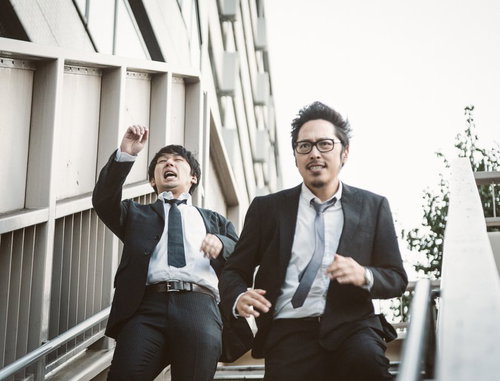 歩道橋の階段を駆け下りるジャーナリストコンビ