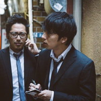 夜間の街で聞き込み取材する操作委員と記者の写真