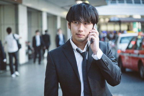 後方のタクシーに気づかず電話で配車手配をするビジネスパーソンの写真