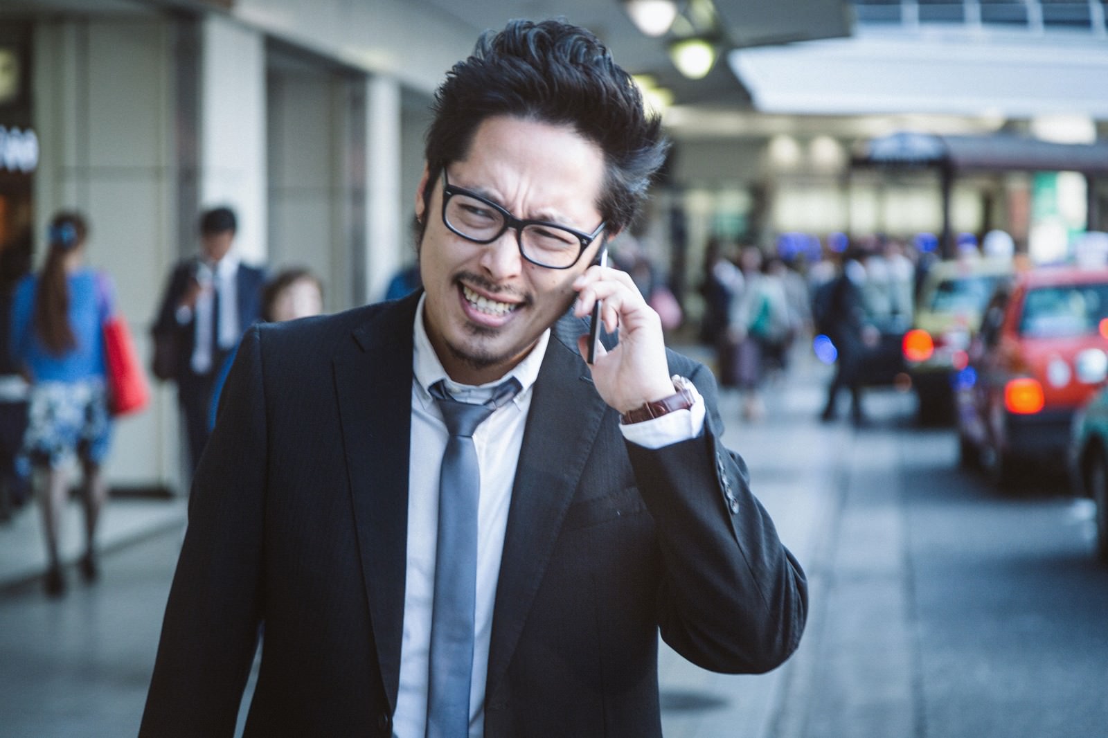 スーツ姿の男性がスマートフォンで電話しながら怒った表情で話している［モデル：ゆうせい］