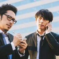 アナログな記者とデジタルなライター、ビルを背景に取材の写真