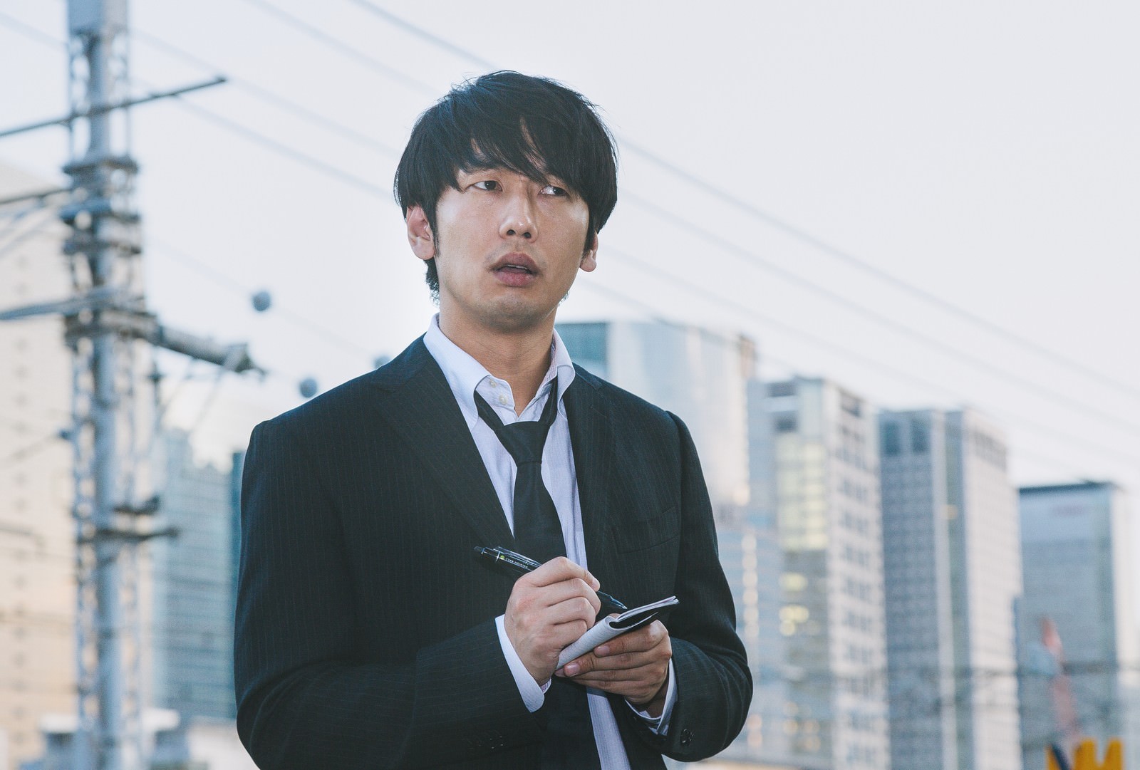 都会でスマートフォンを確認するスーツ姿の男性ジャーナリスト［モデル：大川竜弥］