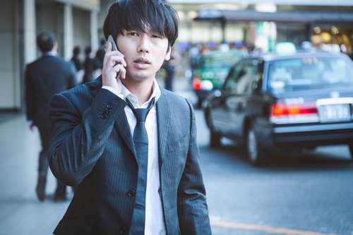 出張帰りタクシーを呼び出しながら待つビジネスマン