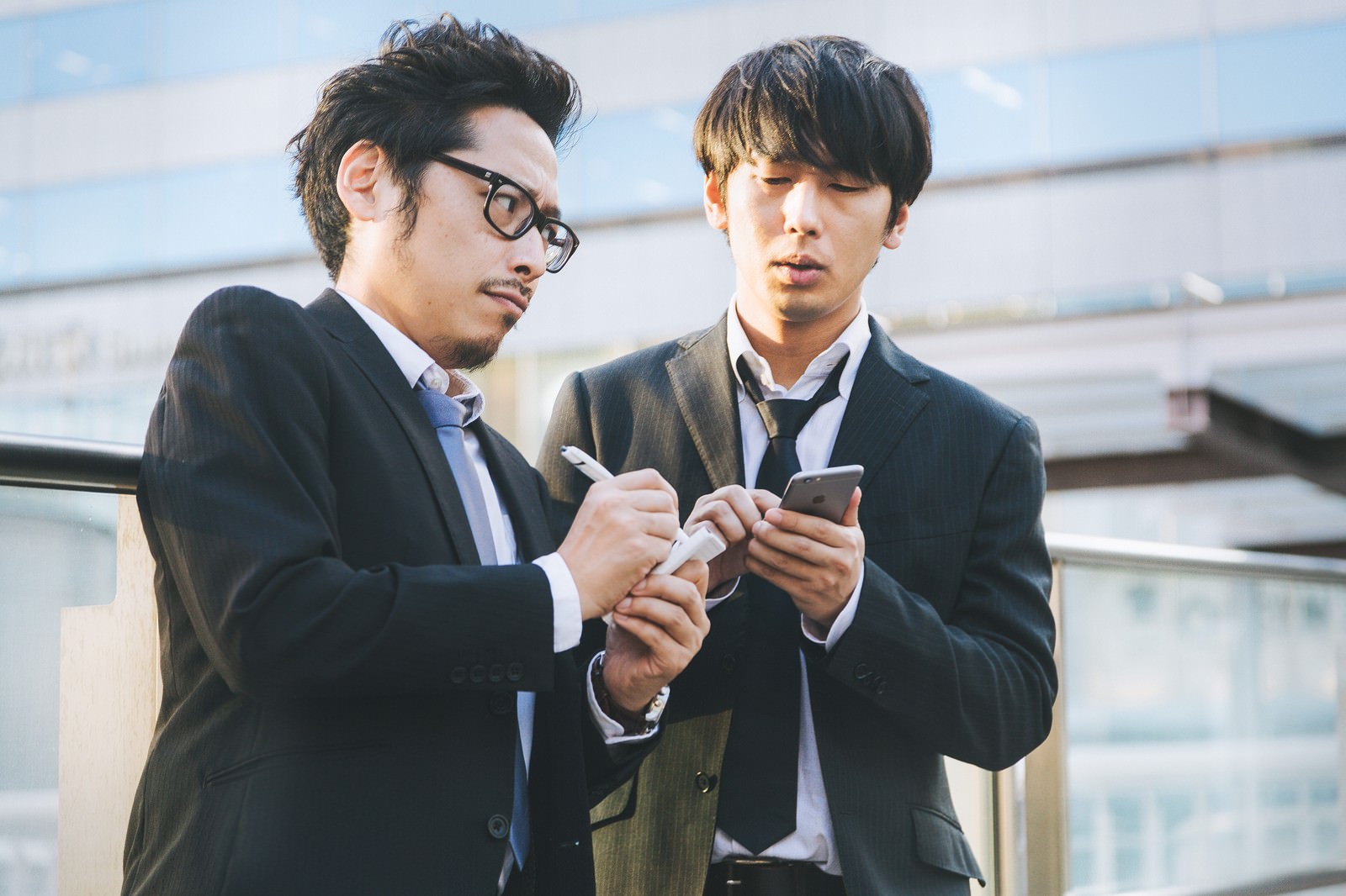 スマートフォンを見ながら手帳にメモを取る2人の男性ジャーナリスト［モデル：ゆうせい 大川竜弥］