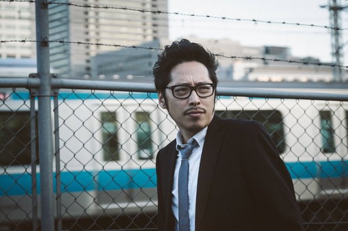 駅前で張り込み調査するジャーナリスト、スーツ姿の男性記者の写真