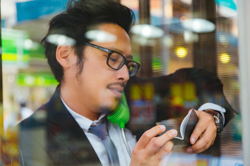 公衆電話で通話しながら自分で書いたメモが読めない男性