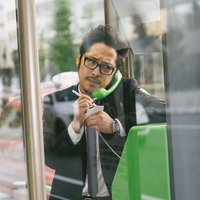 スマホの充電が切れ仕方なく公衆電話で取材を続ける男性ジャーナリストの写真