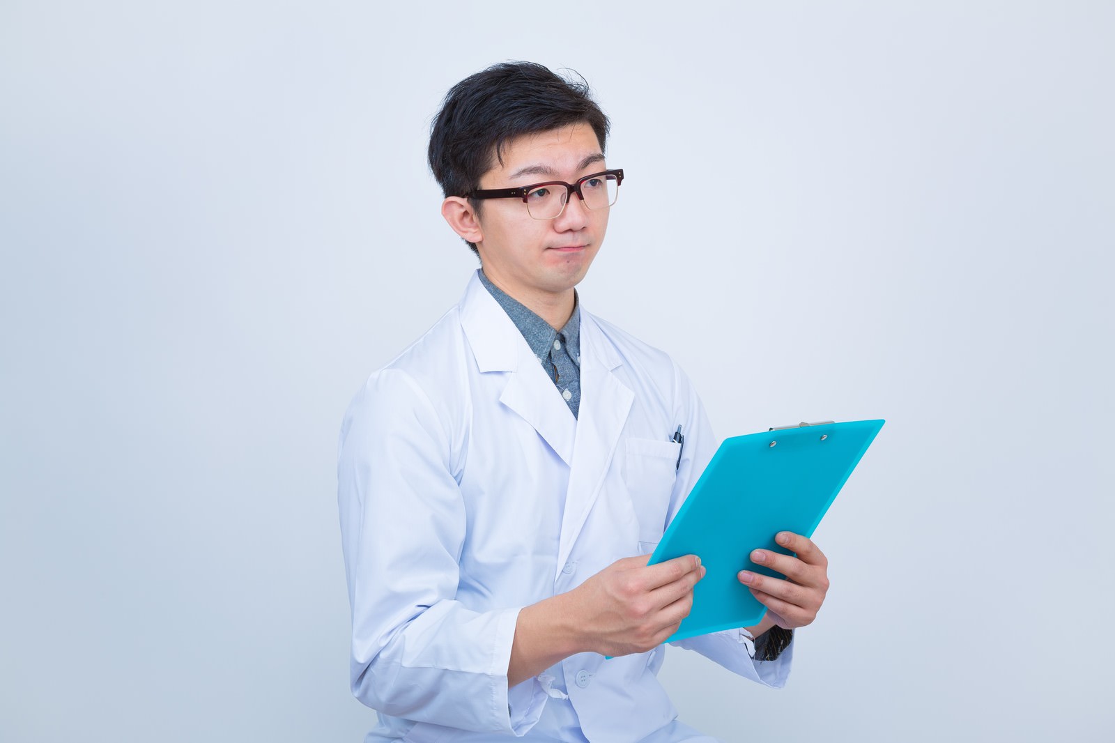 白衣を着た眼鏡をかけた男性医師が青いクリップボードを持っている［モデル：OZPA］