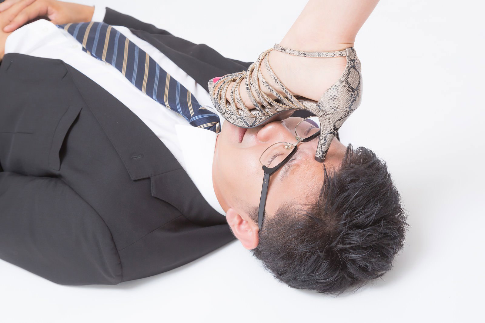 顔の上にヘビ柄ハイヒールを載せられた仰向けの男性［モデル：OZPA］