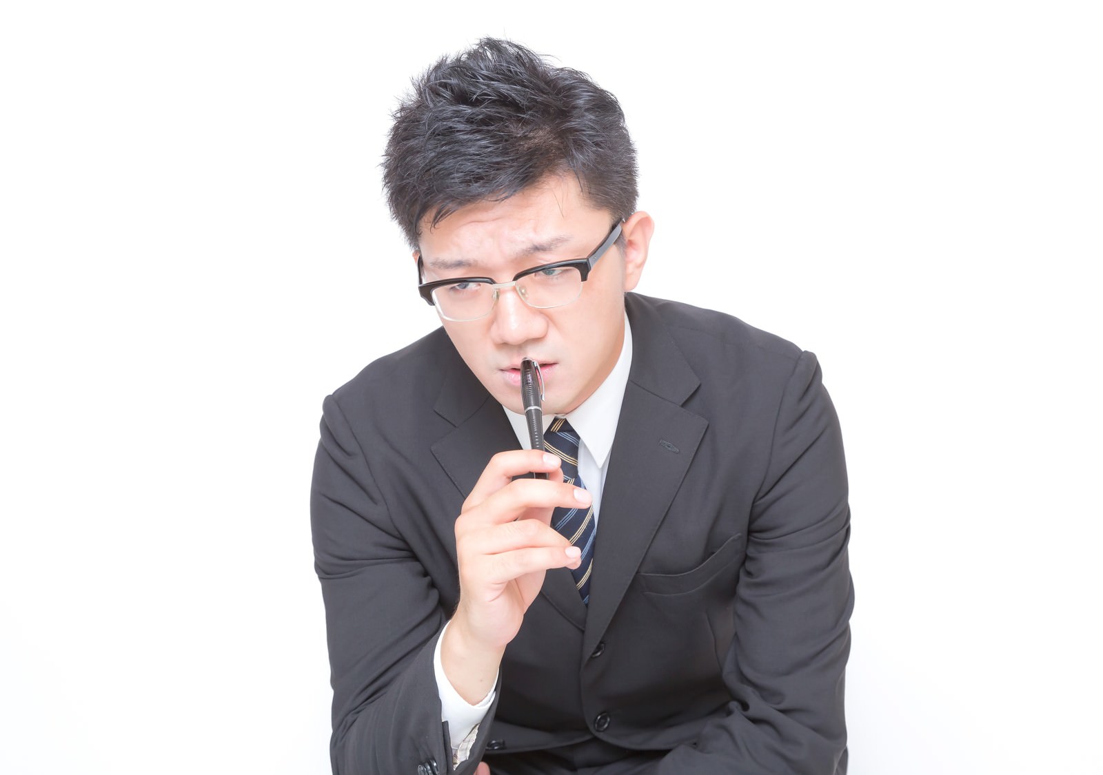 ペンを口元に当てて鬼の形相で睨むビジネスマン［モデル：OZPA］