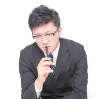 鬼の形相でペンを口元に当てるビジネスマンの写真