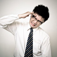 額に手を当てて歯を見せるメガネのビジネスマンの写真