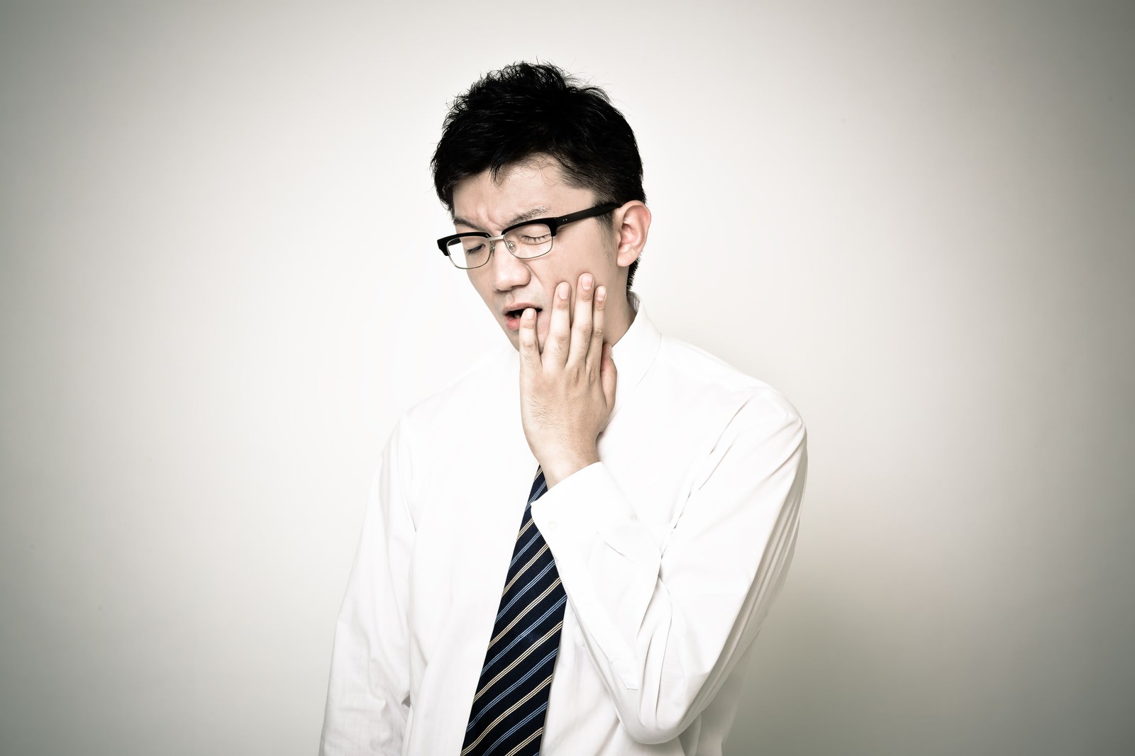 歯の痛みで顔をしかめるスーツ姿の男性［モデル：OZPA］