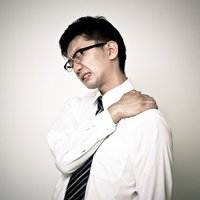 右手で左肩を押さえて顔をしかめる肩こりのスーツ男性の写真