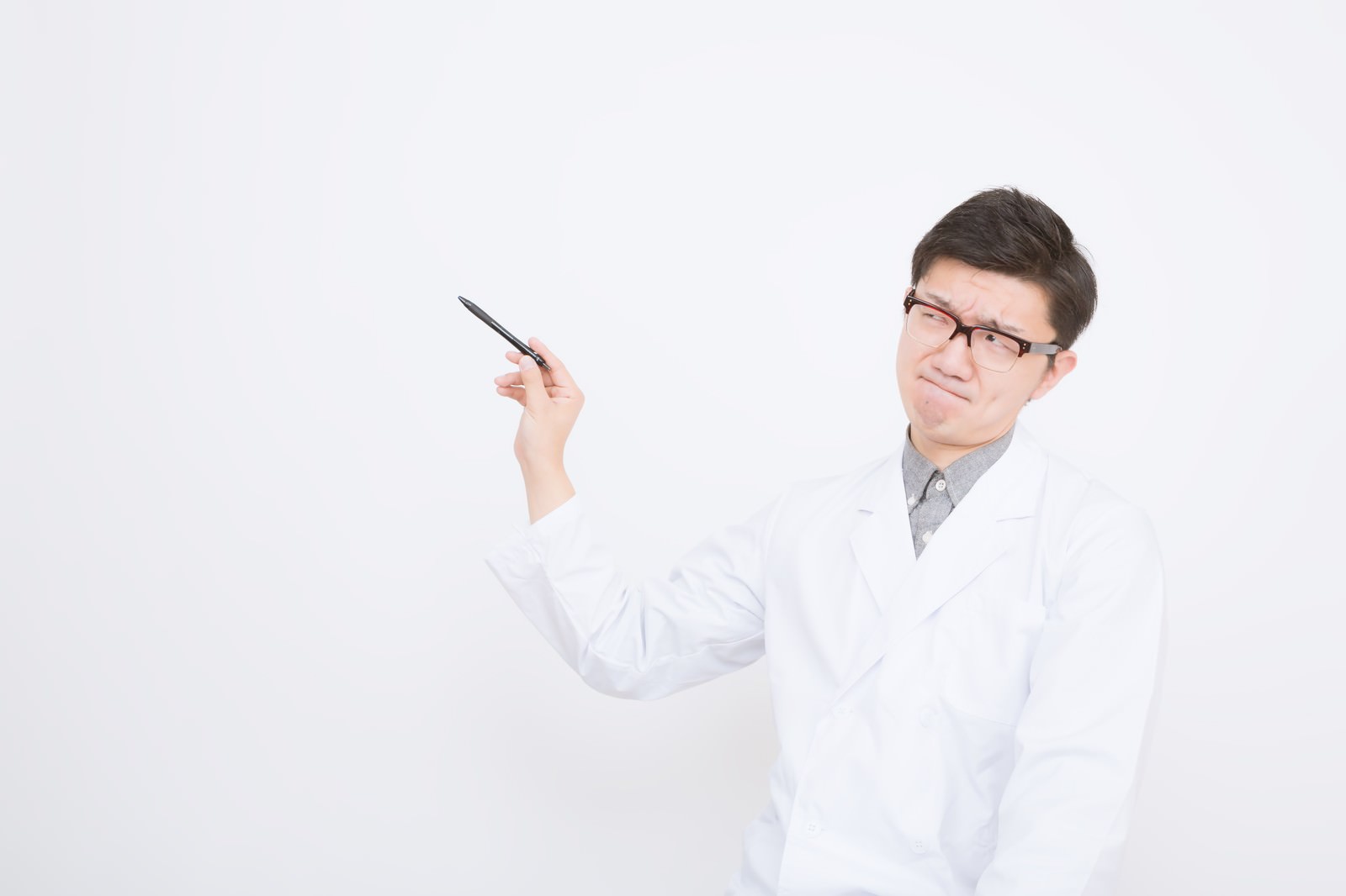 ペンを持ち上げて左を見る白衣の眼鏡の医師［モデル：OZPA］