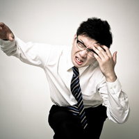 額に手を当て右手を伸ばす頭痛顔の眼鏡の会社員の写真