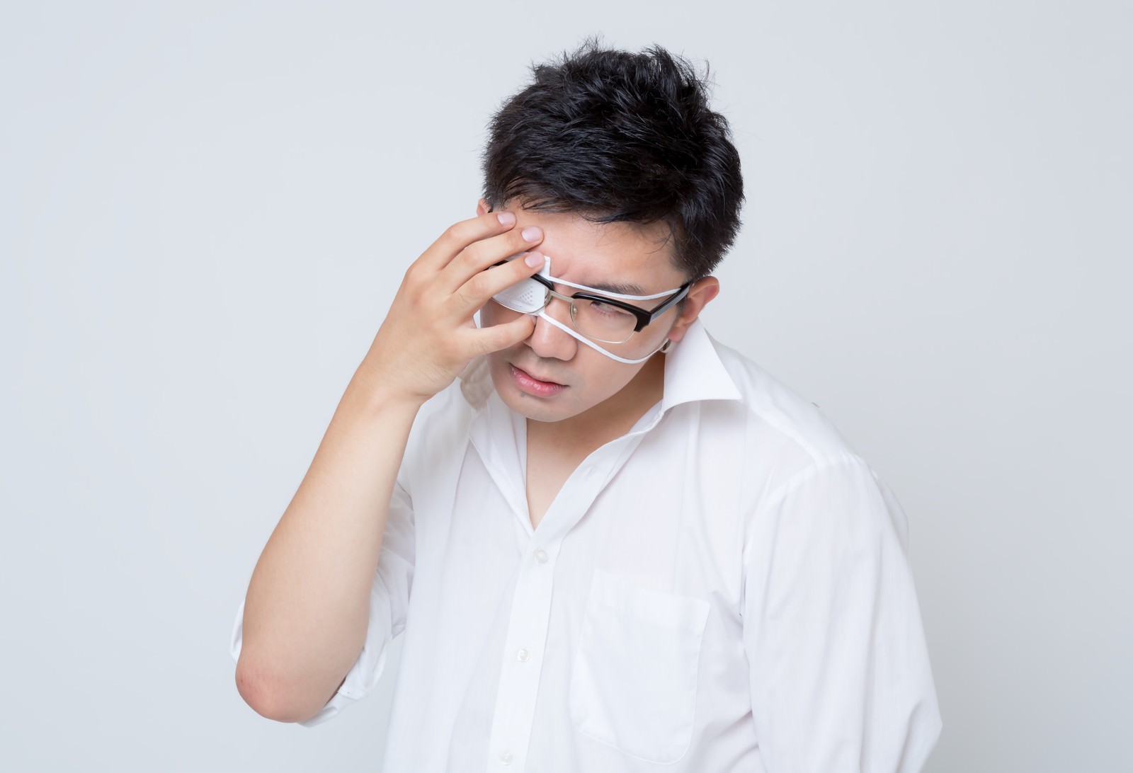 眼鏡型の眼帯をずり上げながら目をおさえる白シャツの男性［モデル：OZPA］