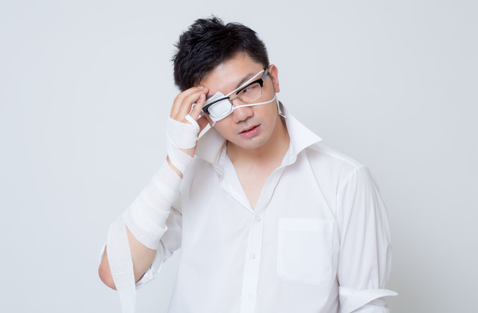 包帯を巻いた腕でメガネを調整する真剣な表情のサラリーマン男性
