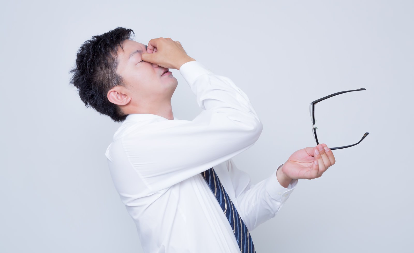 眼精疲労で目をおさえるビジネスマン［モデル：OZPA］