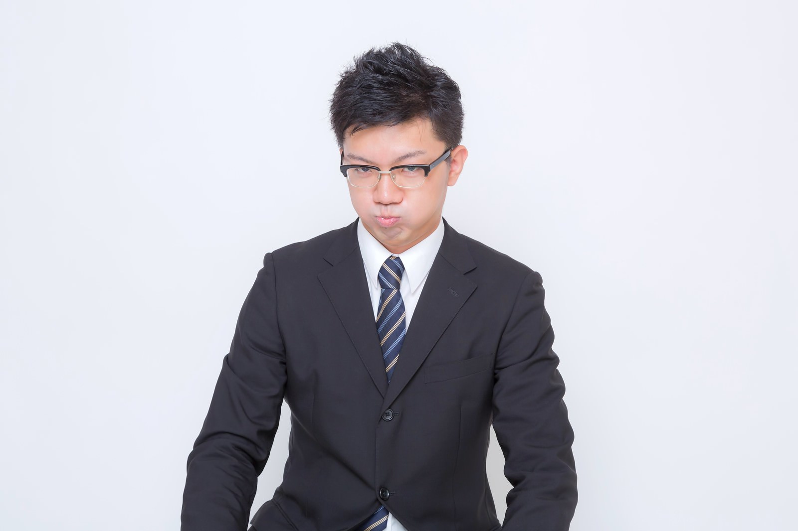 頬をふくらませて口を尖らせるスーツの眼鏡の男性［モデル：OZPA］