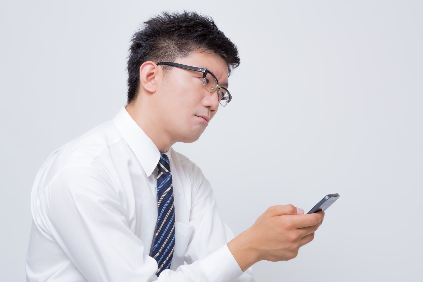 スマホを見ながらイライラする眼鏡をかけた会社員男性［モデル：OZPA］