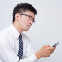 スマートフォンの画面を見てイライラするビジネスマンの写真