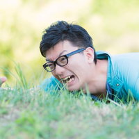 芝生にうつ伏せで手を伸ばす作業服の男性の写真