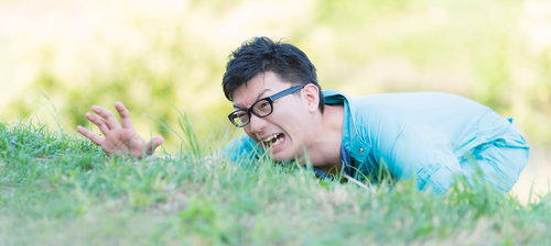 芝生にうつ伏せで手を伸ばす作業服の男性