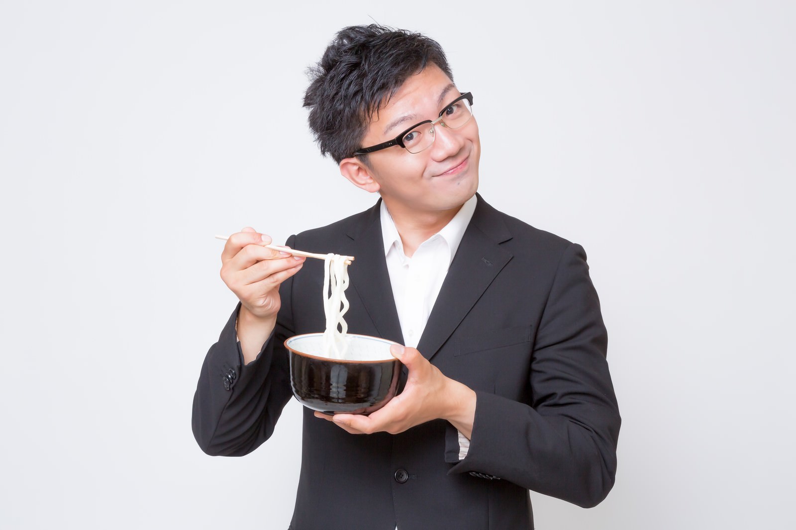 黒縁眼鏡をかけたスーツ姿のビジネスマンが素うどんをすくい上げている［モデル：OZPA］