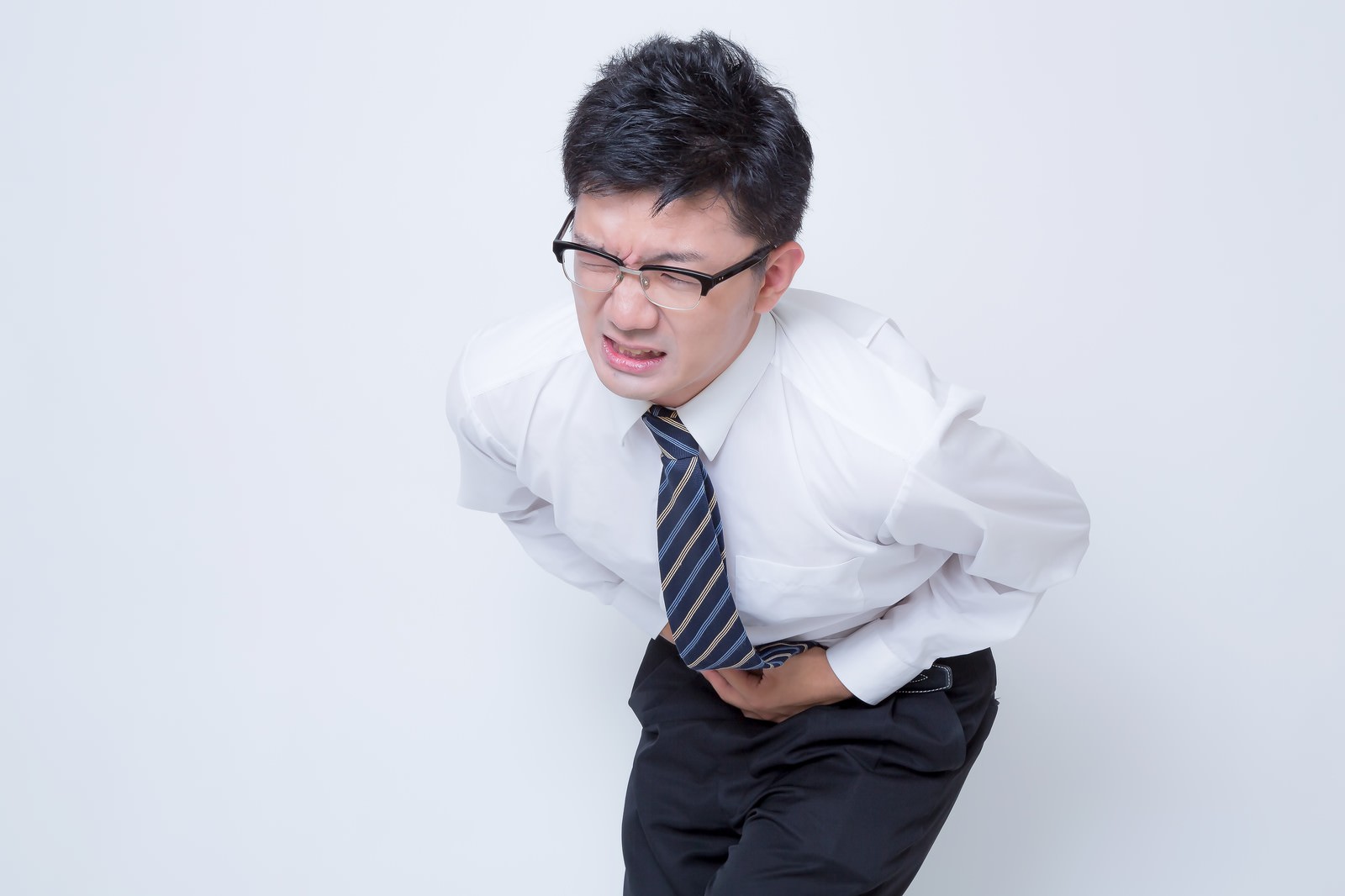 腹痛で前かがみになるスーツの男性［モデル：OZPA］