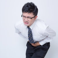 ポンポンペインで前かがみになるサラリーマンの写真