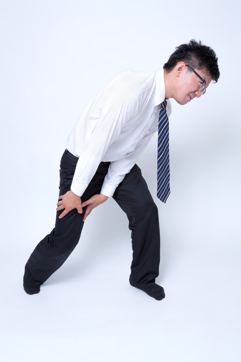 ひざを押さえて痛がるスーツ姿の男性［モデル：OZPA］