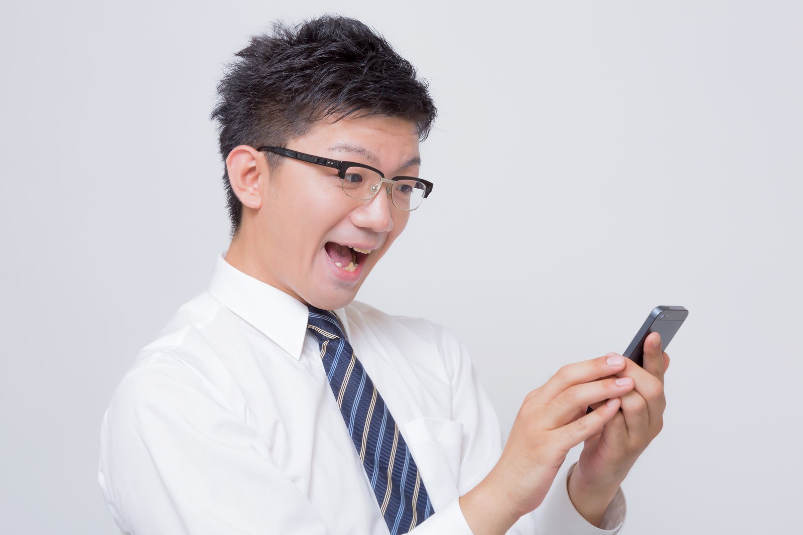 スマホを両手で持って驚いた表情のサラリーマン［モデル：OZPA］