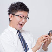 スマホを操作して驚くサラリーマンの写真
