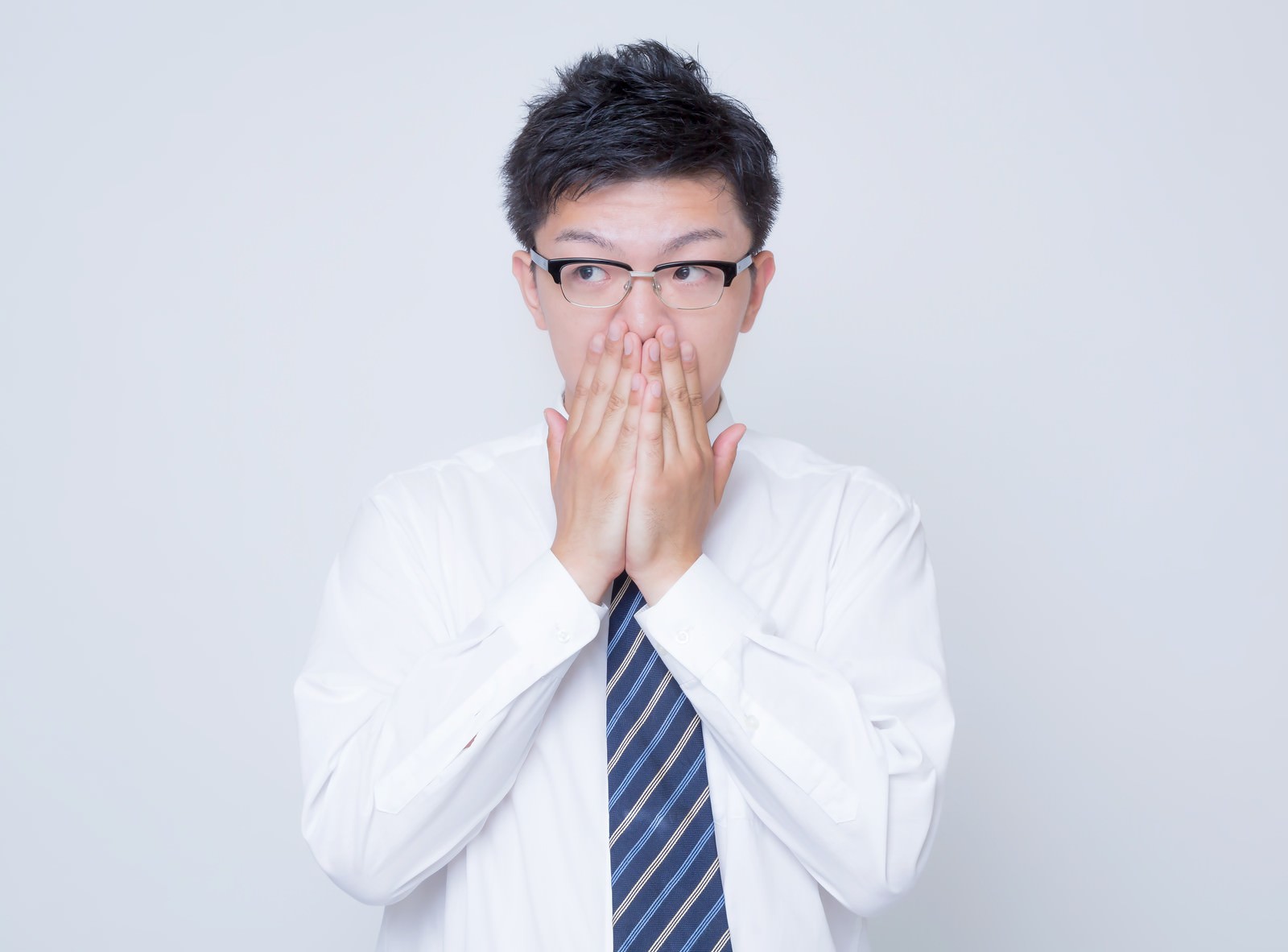 口を両手で覆いながら驚いた表情の眼鏡をかけたビジネスマン［モデル：OZPA］