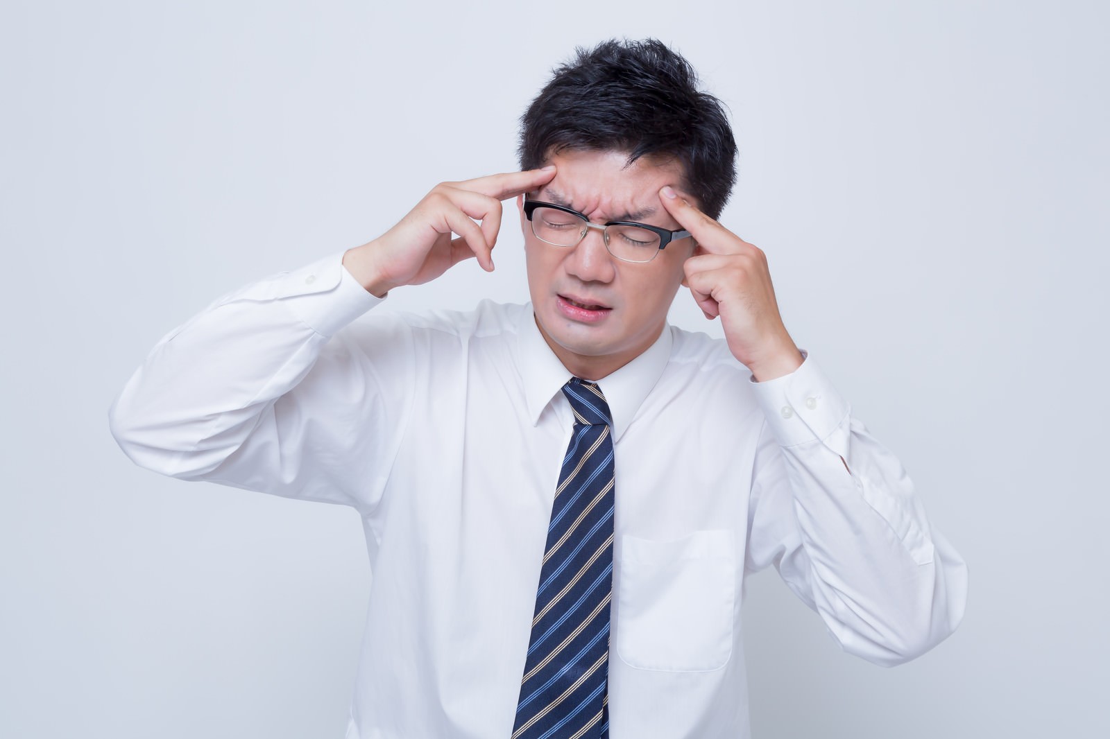 眼鏡をかけた男性が頭痛で眉間を押さえている［モデル：OZPA］
