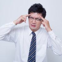 こめかみを押さえて頭痛に耐えるビジネスマンの写真