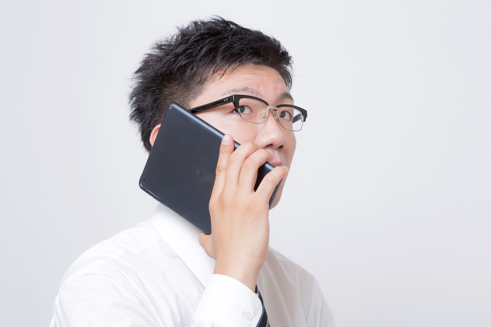 黒いタブレットを耳に当てて通話する眼鏡のサラリーマン［モデル：OZPA］