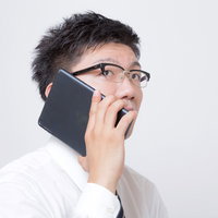 iPadを電話機として耳に当てるサラリーマンの写真